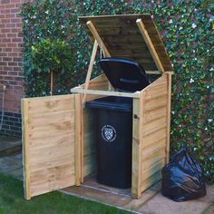 a large wooden trash can sitting next to a black garbage bag on the side of a building