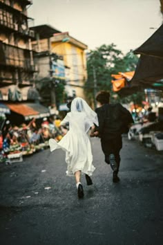 two people are walking down the street in their wedding attire and veils, one person is holding hands with the other