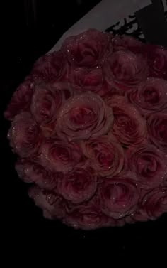 a bouquet of pink roses sitting on top of a black tablecloth with water droplets