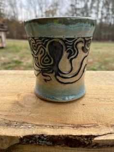 a ceramic cup sitting on top of a wooden table in front of a grassy field