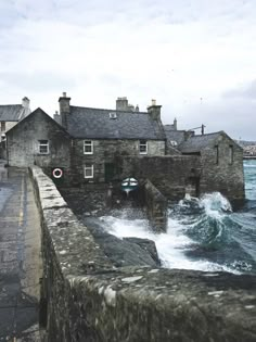 an old stone building sitting next to the ocean with waves crashing in front of it