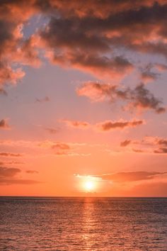 the sun is setting over the ocean on a cloudy day