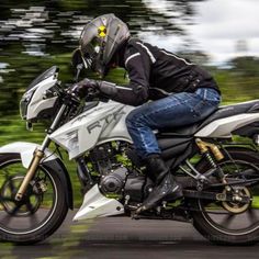 a man riding on the back of a white motorcycle down a street next to trees