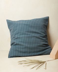 a blue pillow sitting on top of a white table next to a wooden block and plant