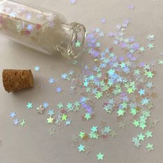 a bottle filled with glitter next to a cork and star shaped confetti sprinkles