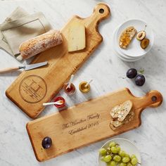 two wooden cutting boards sitting on top of a table with cheese and grapes next to each other