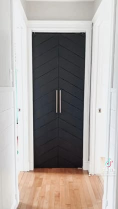 a black door with two brass handles in a white room next to hardwood flooring