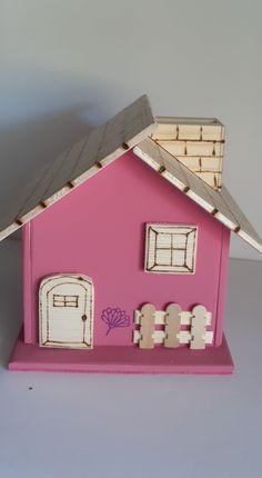 a pink doll house with white picket fence and windows on the front, sitting on a gray surface