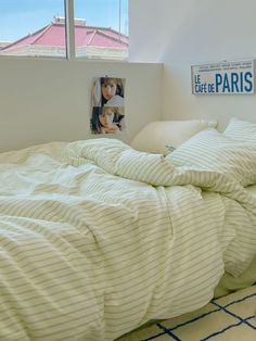 an unmade bed with white sheets and pillows in a room next to a window