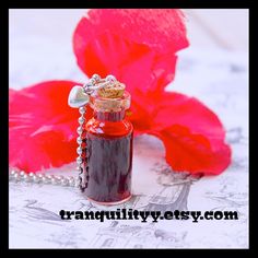 a red flower is sitting next to a small bottle with a tiny charm on it