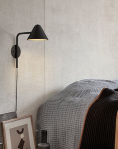 a bed room with a neatly made bed and a wall mounted light on the side