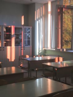 an empty classroom with desks and chairs in front of large windows that have sunlight streaming through them