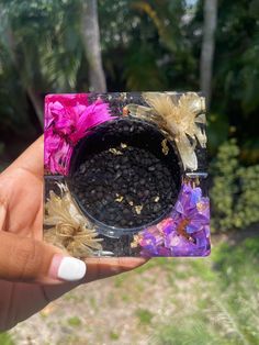 a person holding up a small square object with flowers on it and dirt in the middle