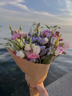 a person holding a bouquet of flowers by the water's edge with their hand