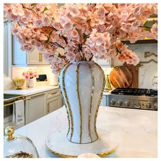 a white vase filled with pink flowers on top of a kitchen counter next to an oven