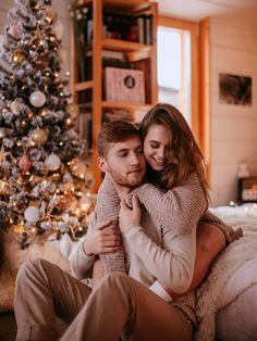 a man and woman cuddle in front of a christmas tree