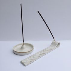 two incense sticks and a bowl on a white surface