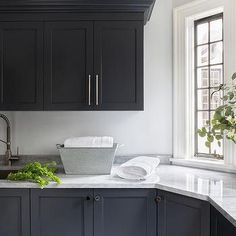 a kitchen with black cabinets and white marble counter tops, along with a sink in the center