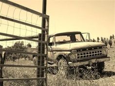 an old truck is parked in the middle of a field near a fence and barbed wire