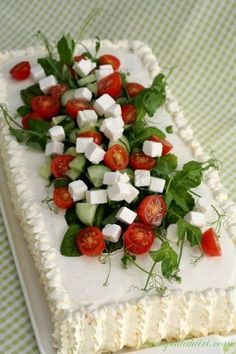 a square cake topped with cucumbers, tomatoes and lettuce on a green checkered tablecloth