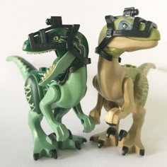 two toy dinosaurs with cameras on their heads, one is green and the other is brown