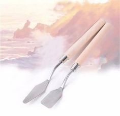 two spatulas with wooden handles are on a white surface next to the ocean