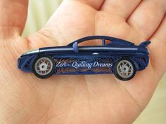 a hand holding a blue car shaped brooch with the words zest quilting dreams written on it