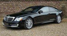 a black car is parked in front of a brick wall and gravel area next to it