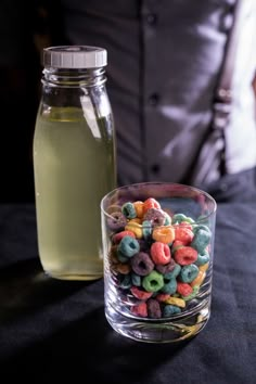 a glass bowl filled with cereal next to a bottle of liquid on a black table