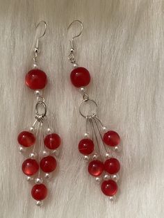 two pairs of red and white beads are hanging from silver earwires on a fur surface