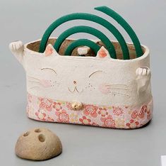 a white cat is sitting in a flowered basket next to a rock and some scissors