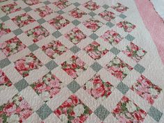 a pink and green quilt with flowers on it's edges is laying on a bed