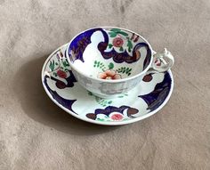 a tea cup and saucer with an ornate design on the rim, sitting on a beige surface