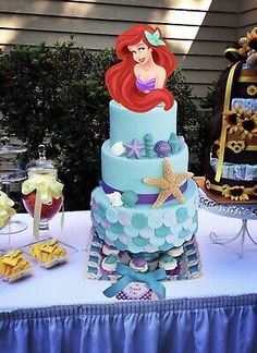 the little mermaid is sitting on top of the blue and green cake at the table