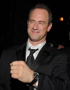 a man in a suit and tie smiling at the camera with his hand on his chest