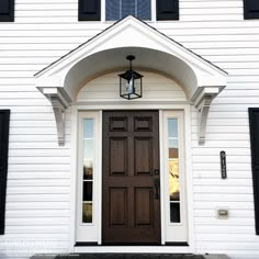 the front door of a white house with black shutters and a lantern on it