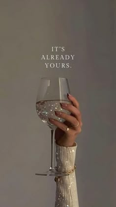 a woman holding a wine glass with the words it's already yours