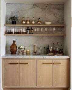 a kitchen with marble counter tops and wooden cabinets, filled with wine glasses on the shelves