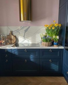 a kitchen with blue cabinets and white marble counter tops, yellow daffodils in vases on the sink