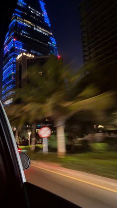 a car driving down the road in front of some tall buildings at night with blue lights