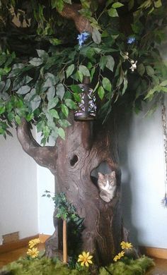 a cat sitting in a tree house made out of branches and leaves with a bird feeder on top