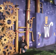 a woman sitting on the ground next to a giant clock made out of gold gears