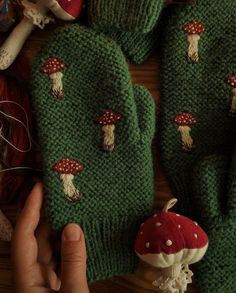 a hand is holding up two knitted mittens with mushrooms on them