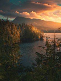 a lake surrounded by trees and mountains under a cloudy sky at sunset in the woods