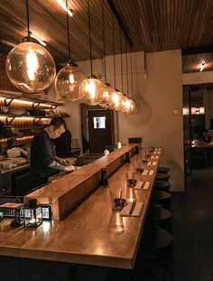 two men sitting at a bar in a restaurant with lights hanging from the ceiling above them