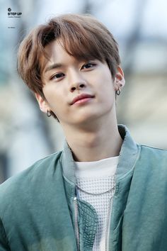 the young man is wearing a green jacket and earrings, looking off to the side