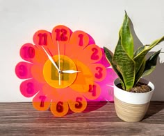 a colorful clock sitting next to a potted plant on top of a wooden table