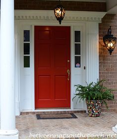 a green front door on a brick house with potted plants and two lights hanging from the ceiling