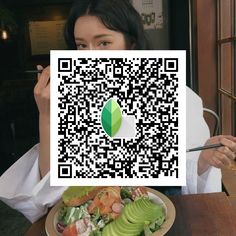 a woman sitting at a table with a plate of food and a qr code