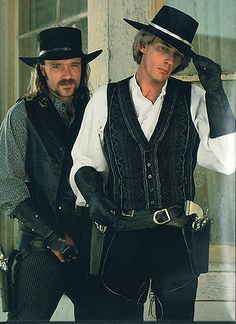 two men in black hats and vests standing next to each other